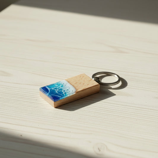 Keychain with wooden back and blue and white resin wave design on a light wood surface