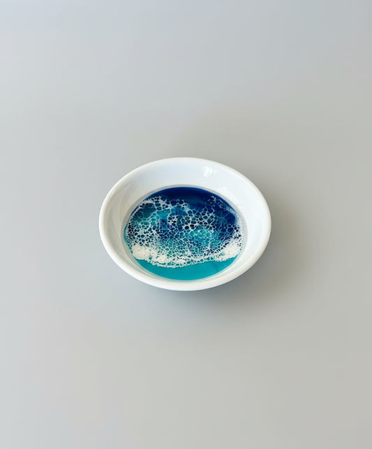 Small white ceramic dish with blue and white resin waves on a light gray background