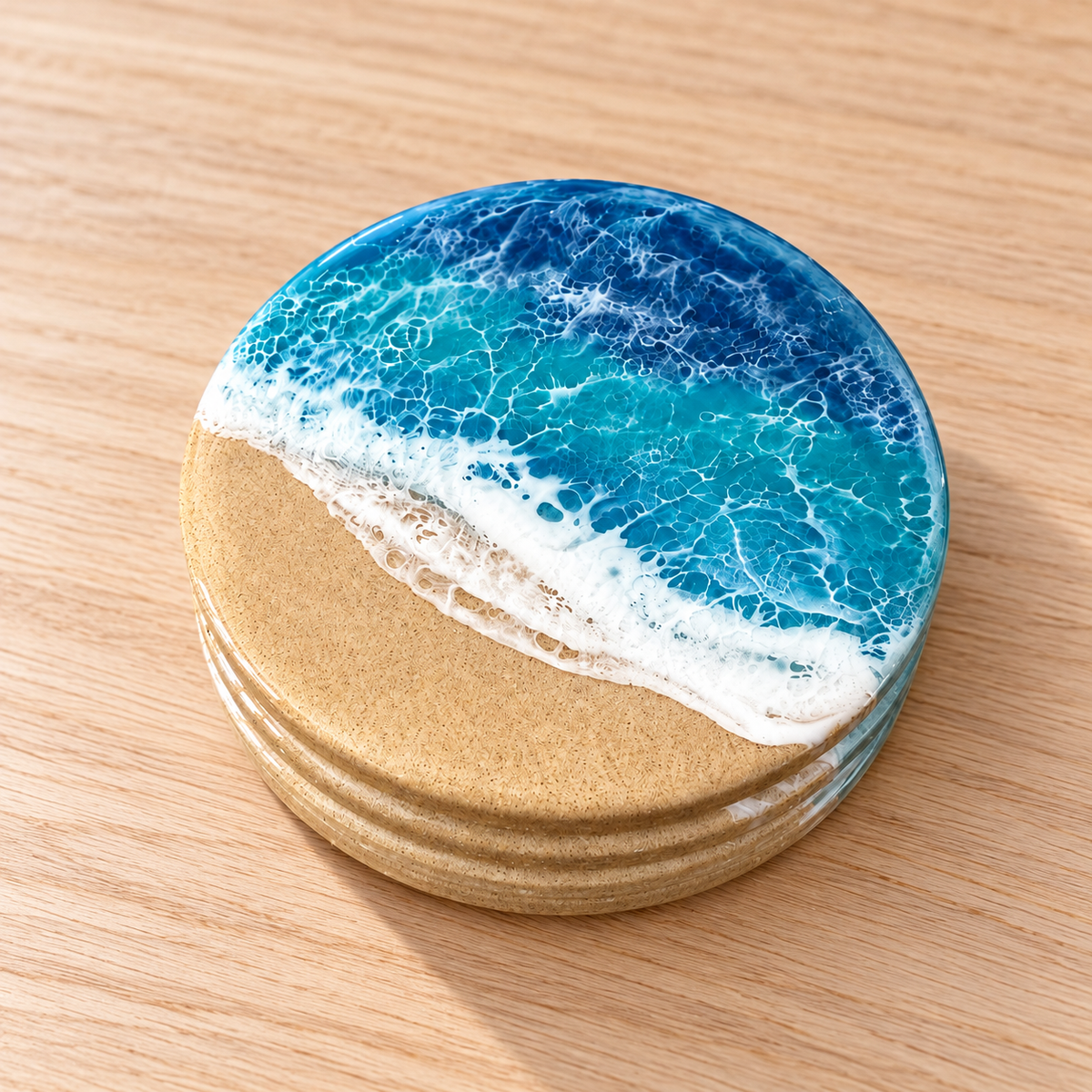 A round coaster with a beach and ocean design, featuring blue and turquoise water with white foam waves and a sandy beige shore, shown on a light wood surface.