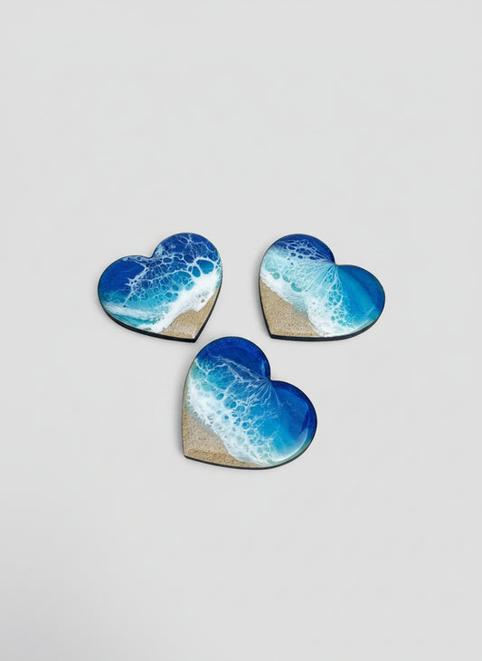 Three heart shaped resin wave magnets with ocean wave design on a light gray background