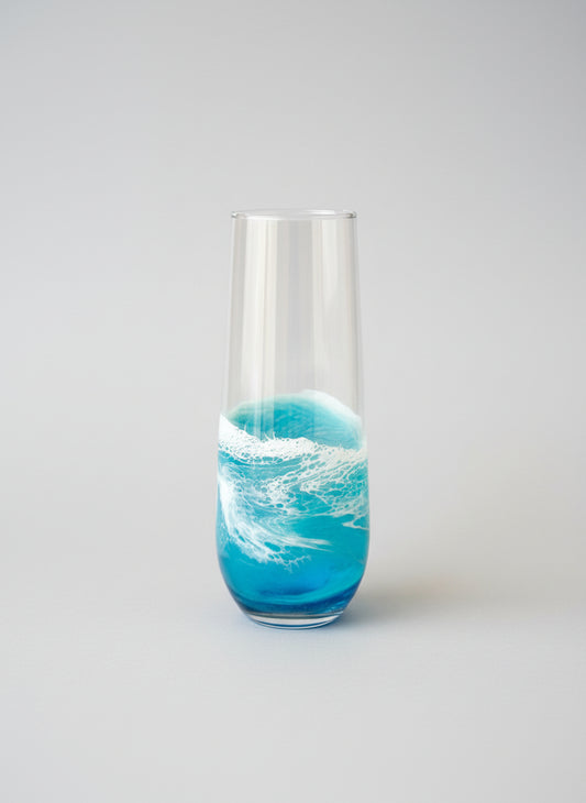 Tall glass with blue liquid and white wave design on a light gray background