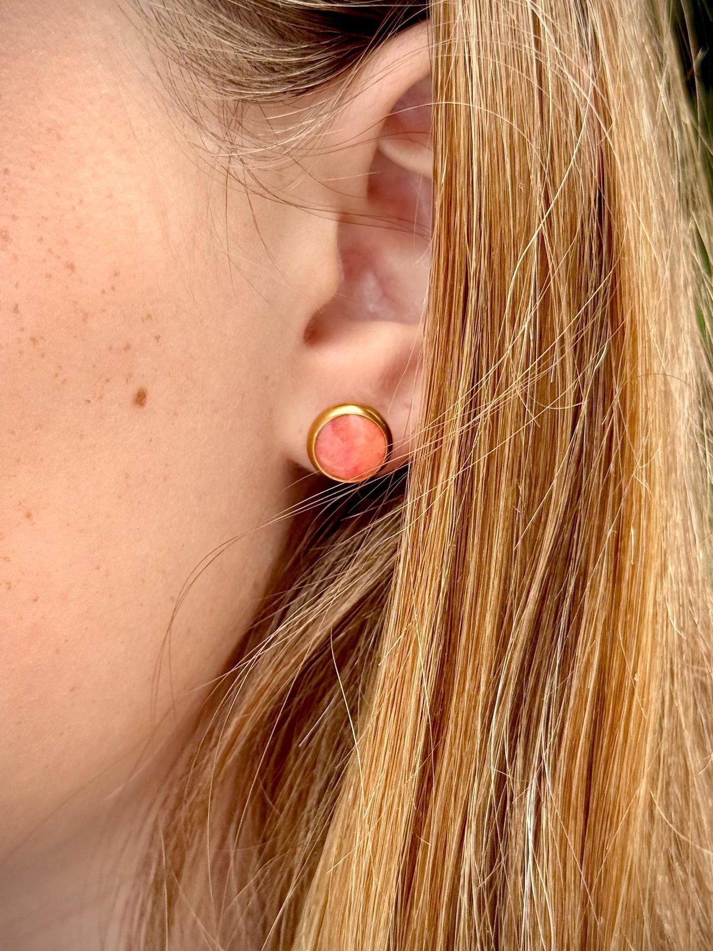 Close-up of a person wearing a round earring with a pink gemstone.