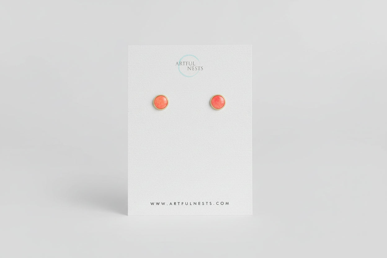 Pair of coral stud earrings on a 'Artful Nests' branded card with green leaves in the background.