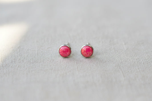 Pink stud earrings on a light gray fabric background
