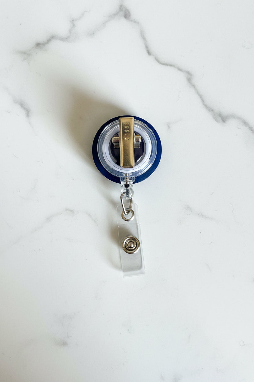 A retractable badge reel with a blue circular body, clear plastic retractor housing, and a clear clip, shown on a textured brown wooden surface.
